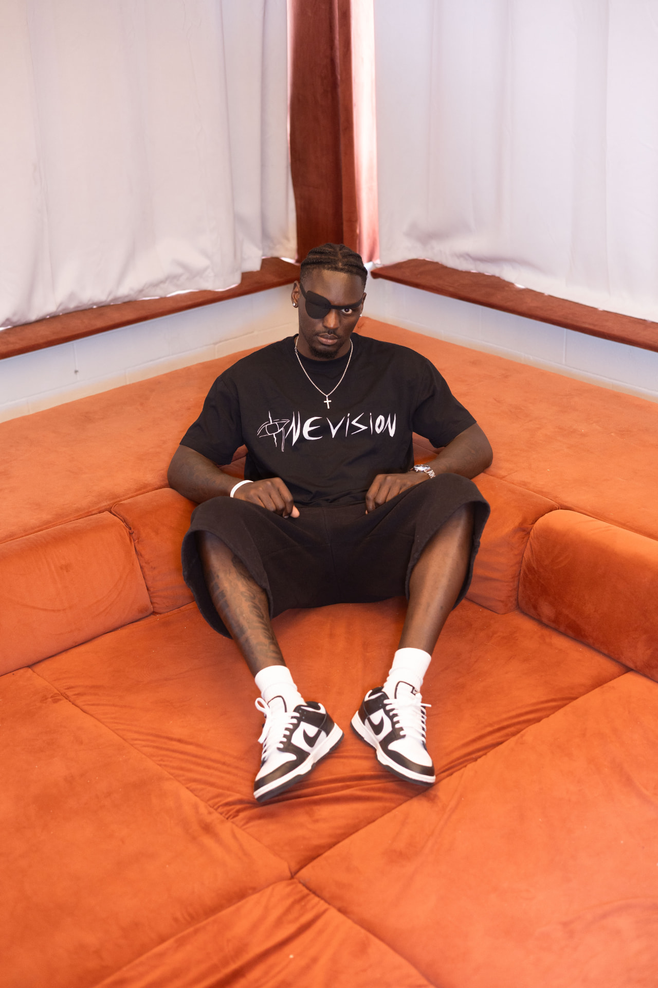 Model in blackout tee and shorts reclining on a burnt orange modular sofa